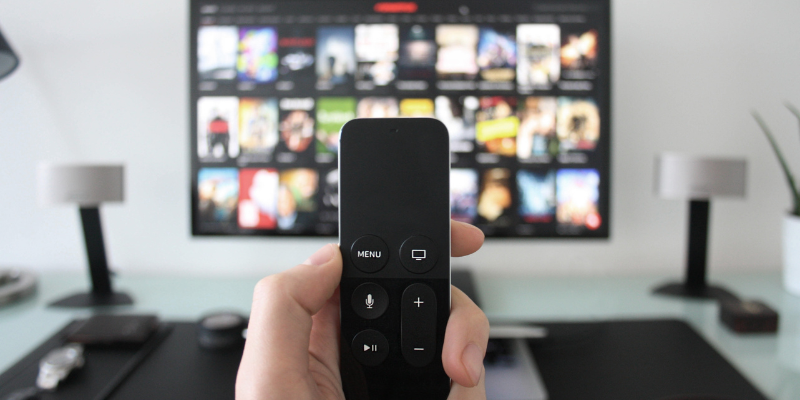 Streaming Services Image of hand holding streaming stick with TV streaming services in the background.