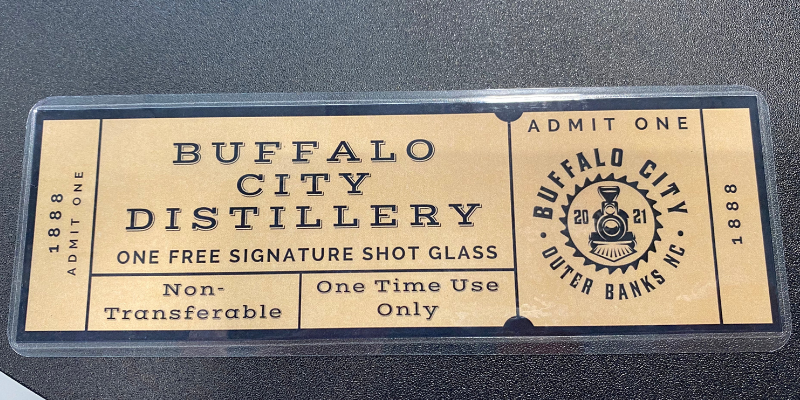 Buffalo City Distillery - Tour A tan laminated ticket with the words "Buffalo City Distillery One Free Signature Shot Glass."