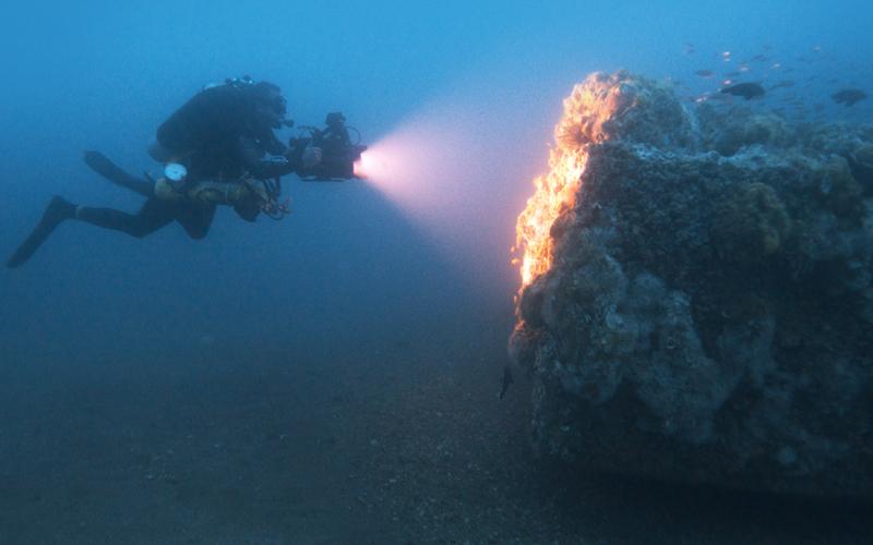 Scuba diver shining a light underwater at a graveyard of the Atlantic shipwreck